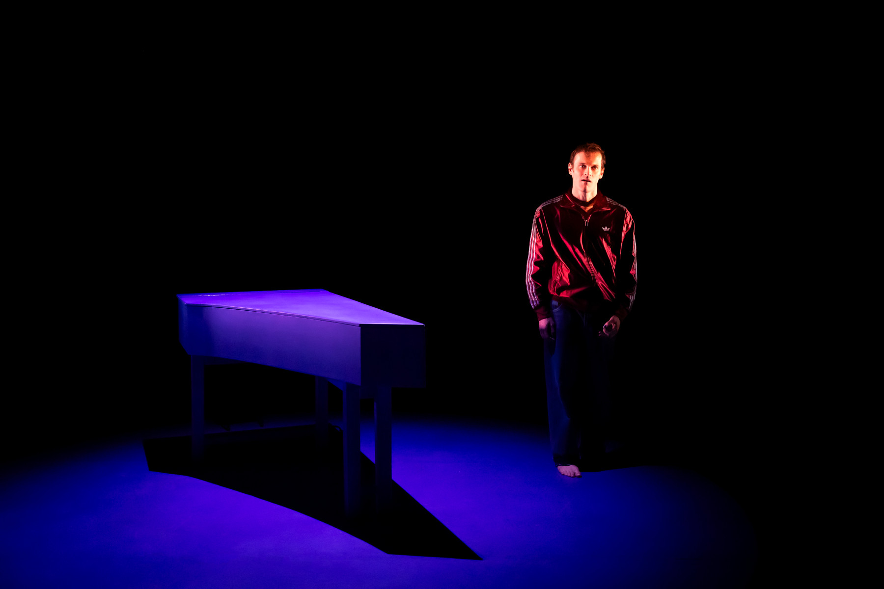 Maxime Taffanel est debout dans un espace bleu Klein, un clavecin bleu à sa droite, lumière franche.