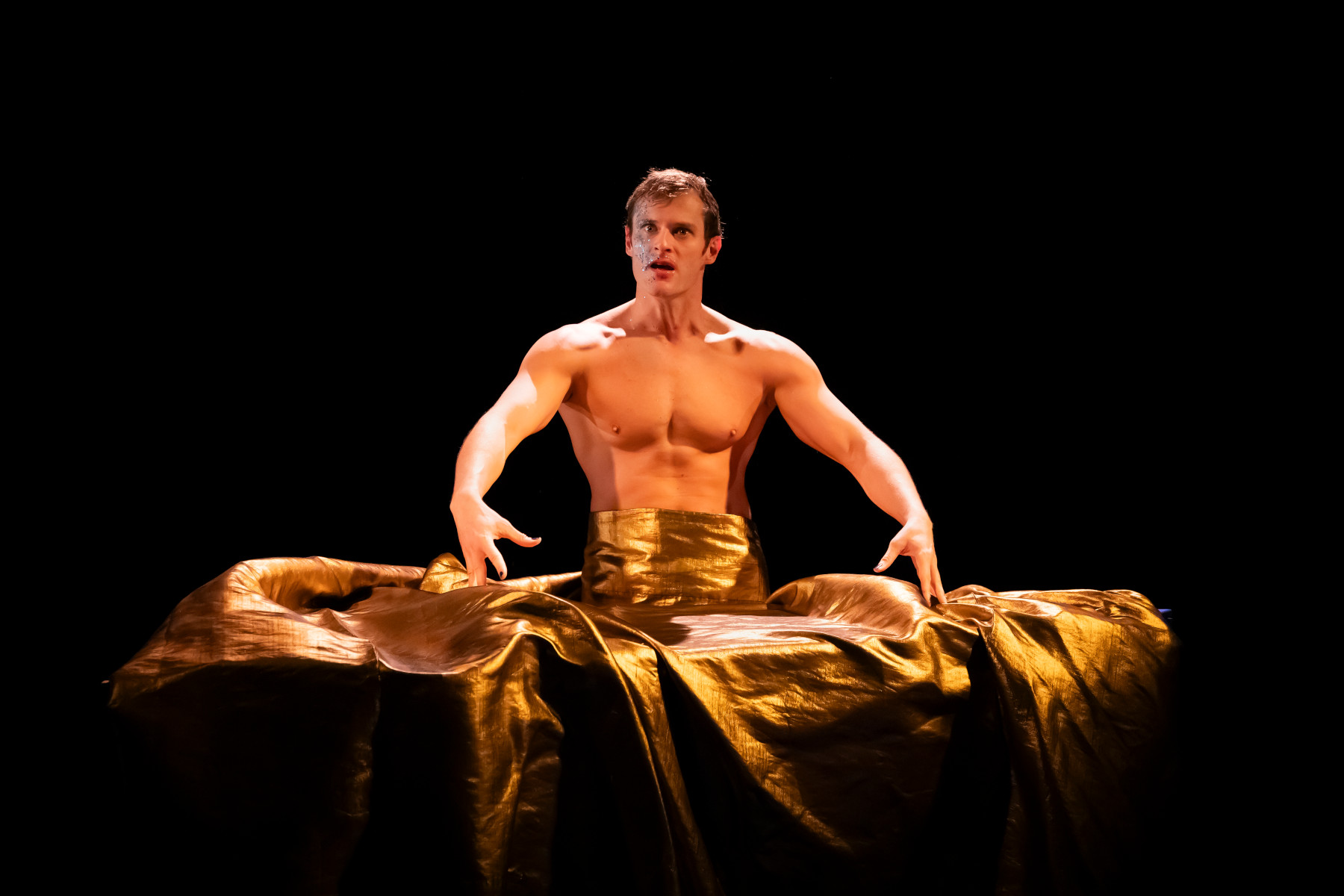 Homme en jupe longue dorée, lumière chaude.