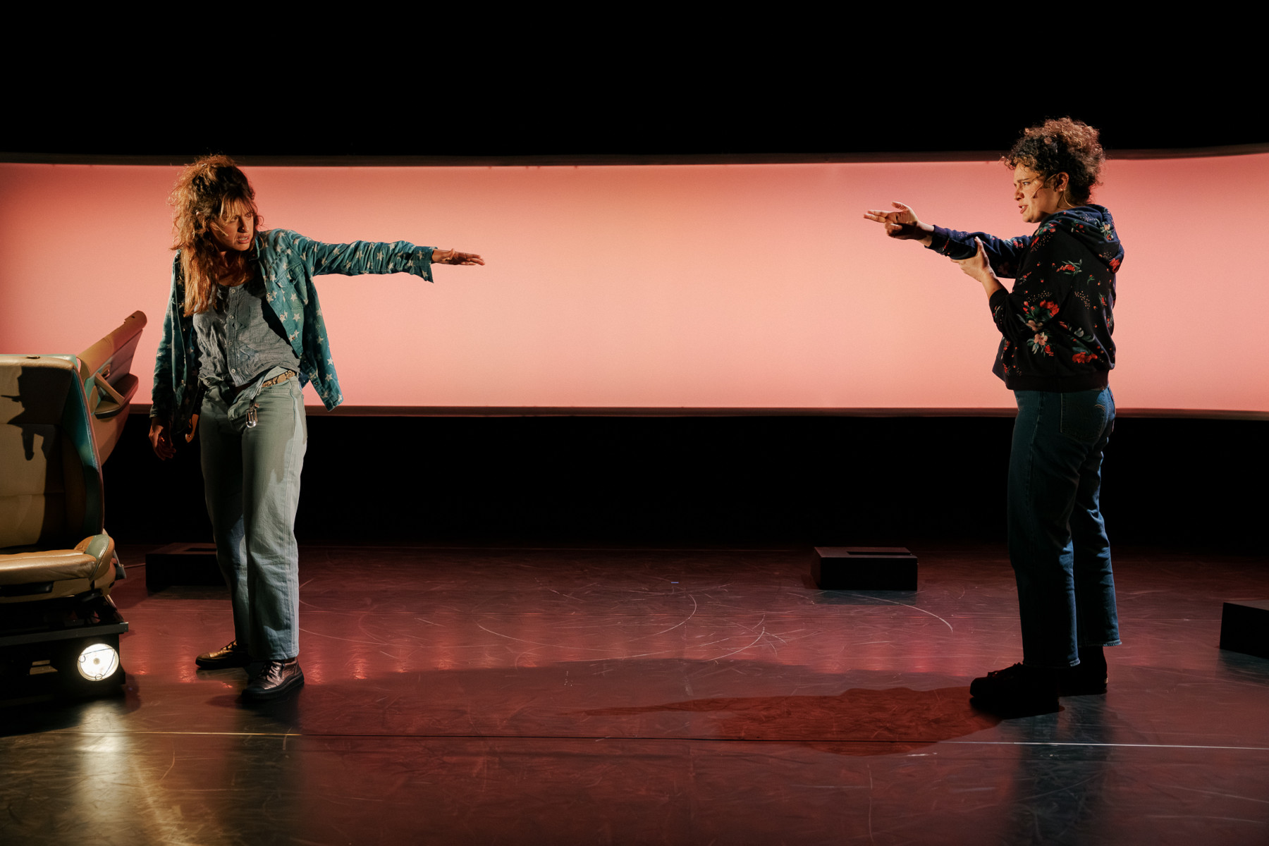 Une femme mime de pointer un revolver sur une autre, lumière chaude et tamisée.