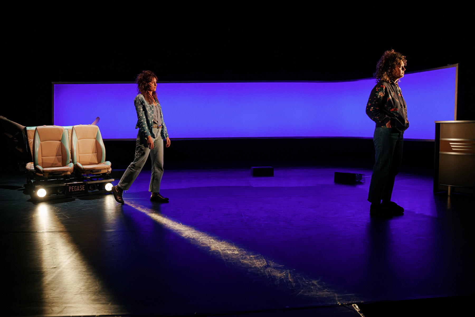 Deux femmes dans une ambiance lumineuse nocturne, phares de voitures qui balaient le sol, cyclo bleu.